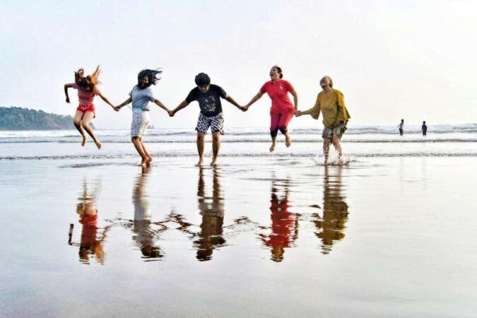 Un groupe d'amis se tenant la main et sautant ensemble sur une plage pour essayer des activités insolites.
