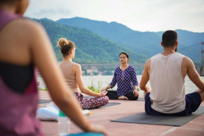 Un groupe de personnes pratique la méditation en plein air face à des montagnes lors d'une retraite de yoga.